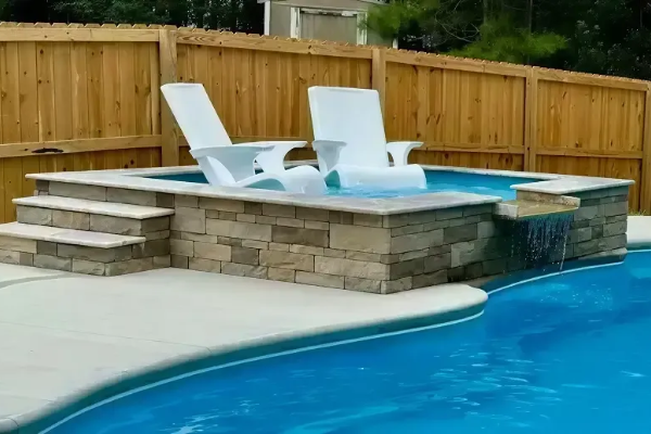 Backyard pool with raised stone spa, white lounge chairs, and a wooden privacy fence