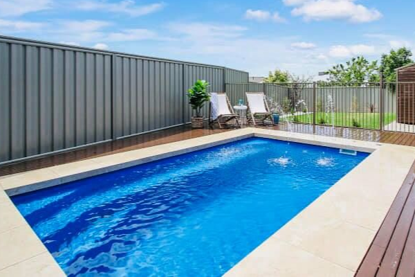 Modern backyard with rectangular blue swimming pool, lounge chairs, and gray privacy fencing