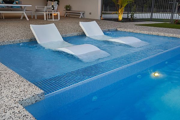 Pool with two white in-water lounge chairs beside a blue swimming pool.