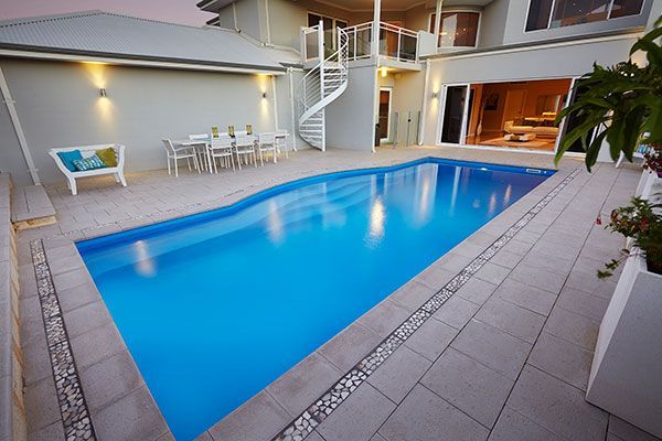 Indoor courtyard with a blue swimming pool, white chairs, and a spiral staircase at a modern home