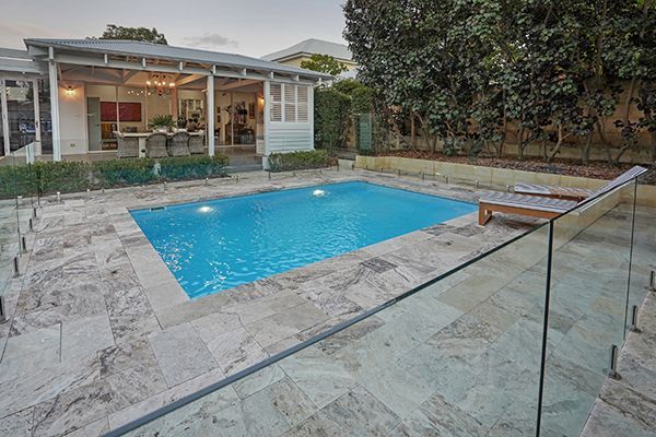 Backyard pool with glass railing and a house patio in the background