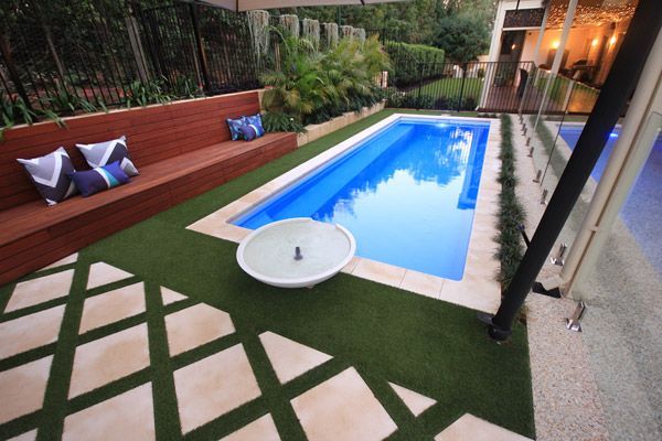 Modern backyard with a rectangular pool, lounge seating, and stone pavers beside green turf.