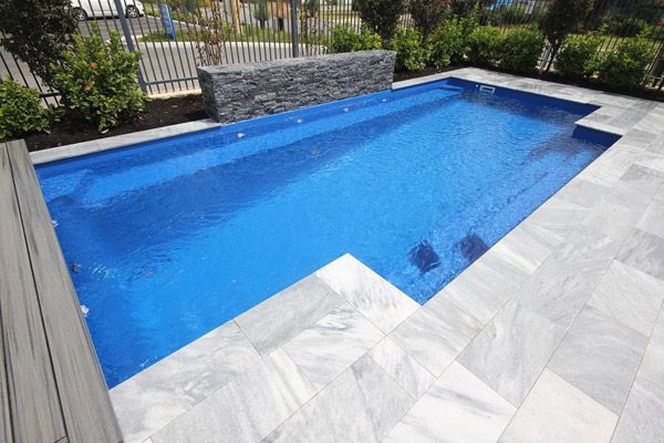 Modern backyard swimming pool with blue water and light gray stone decking