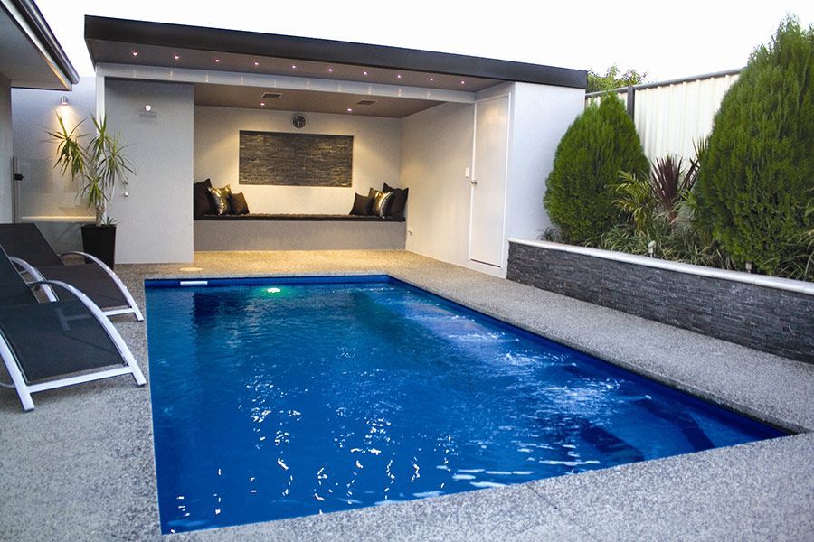Modern backyard pool with blue water, covered patio, lounge chair, and landscaped hedges