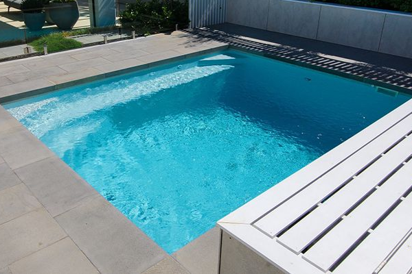 Rectangular outdoor swimming pool with blue water and light stone decking