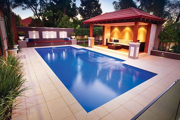 Backyard swimming pool beside a covered patio with red roof and warm lighting at dusk
