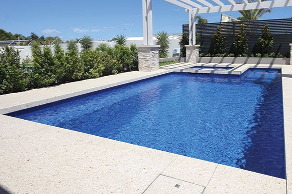 Blue rectangular swimming pool beside a white pergola and landscaped garden under a clear sky