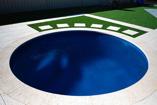 Blue circular pool with a white deck and green decorative border near the top edge