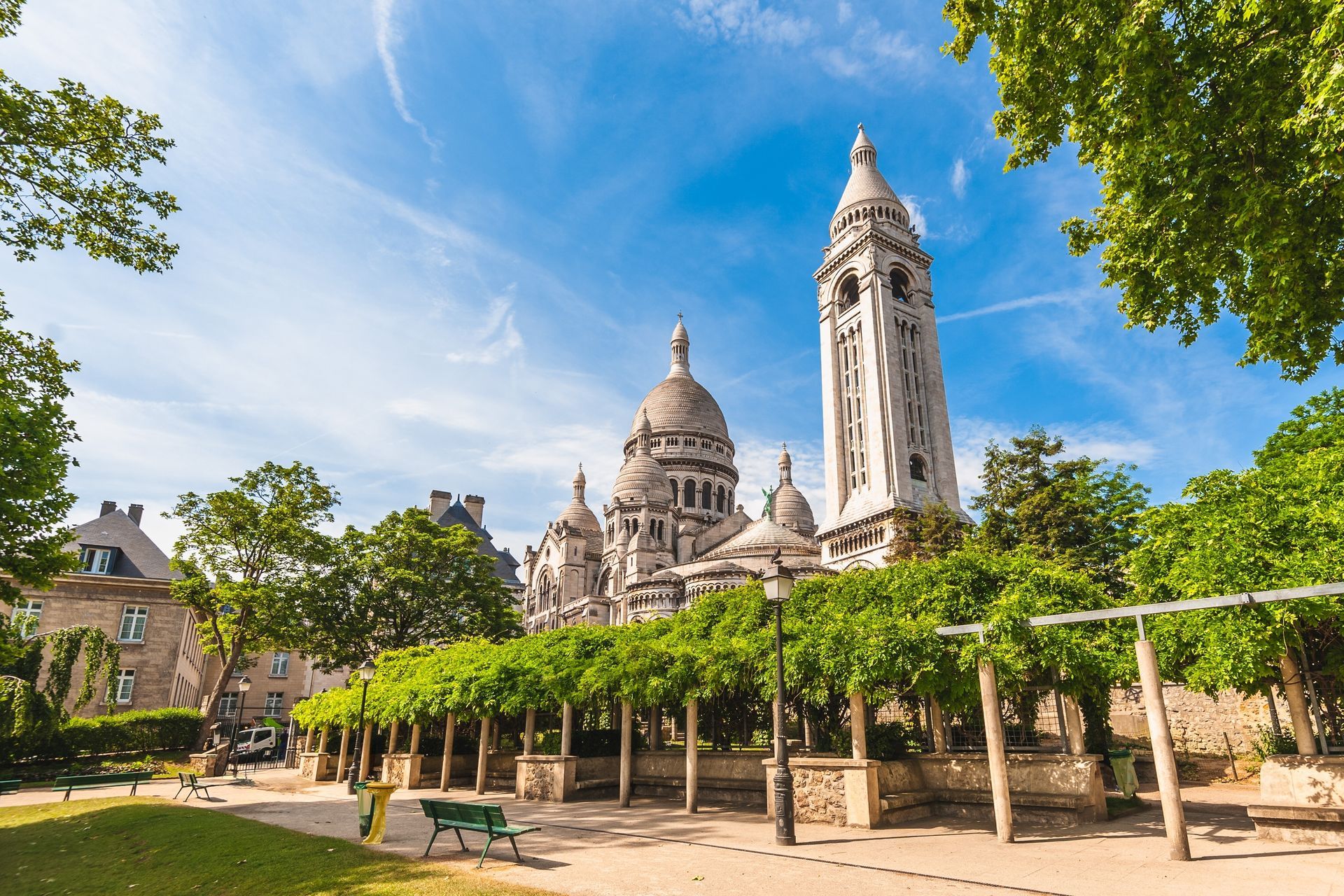 Sacre-Coeur Basilica, Paris, France, on a sunny day, framed by green trees and a public square.