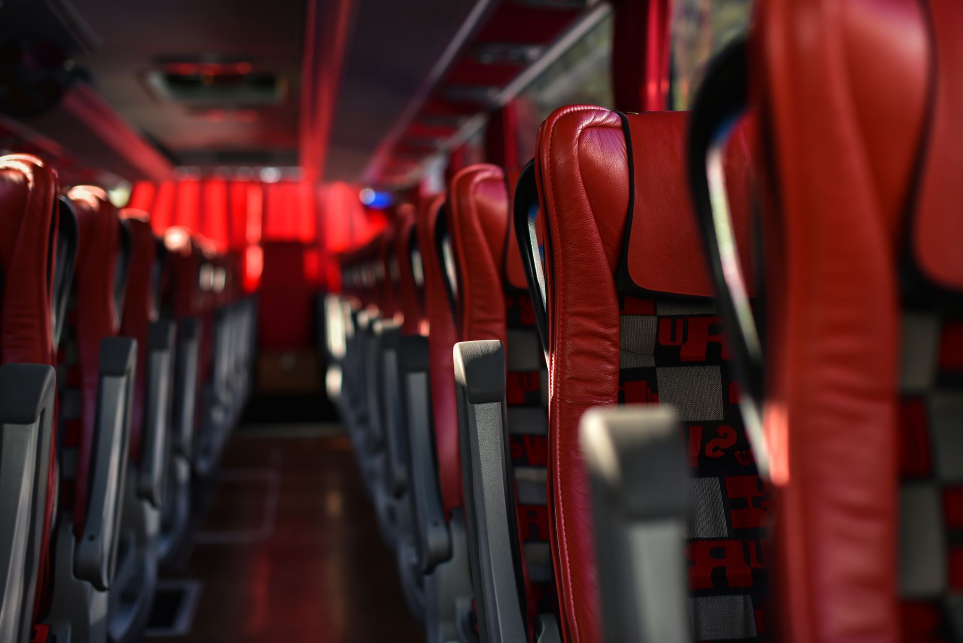 Empty bus interior with rows of red seats, red curtains, and overhead lighting.