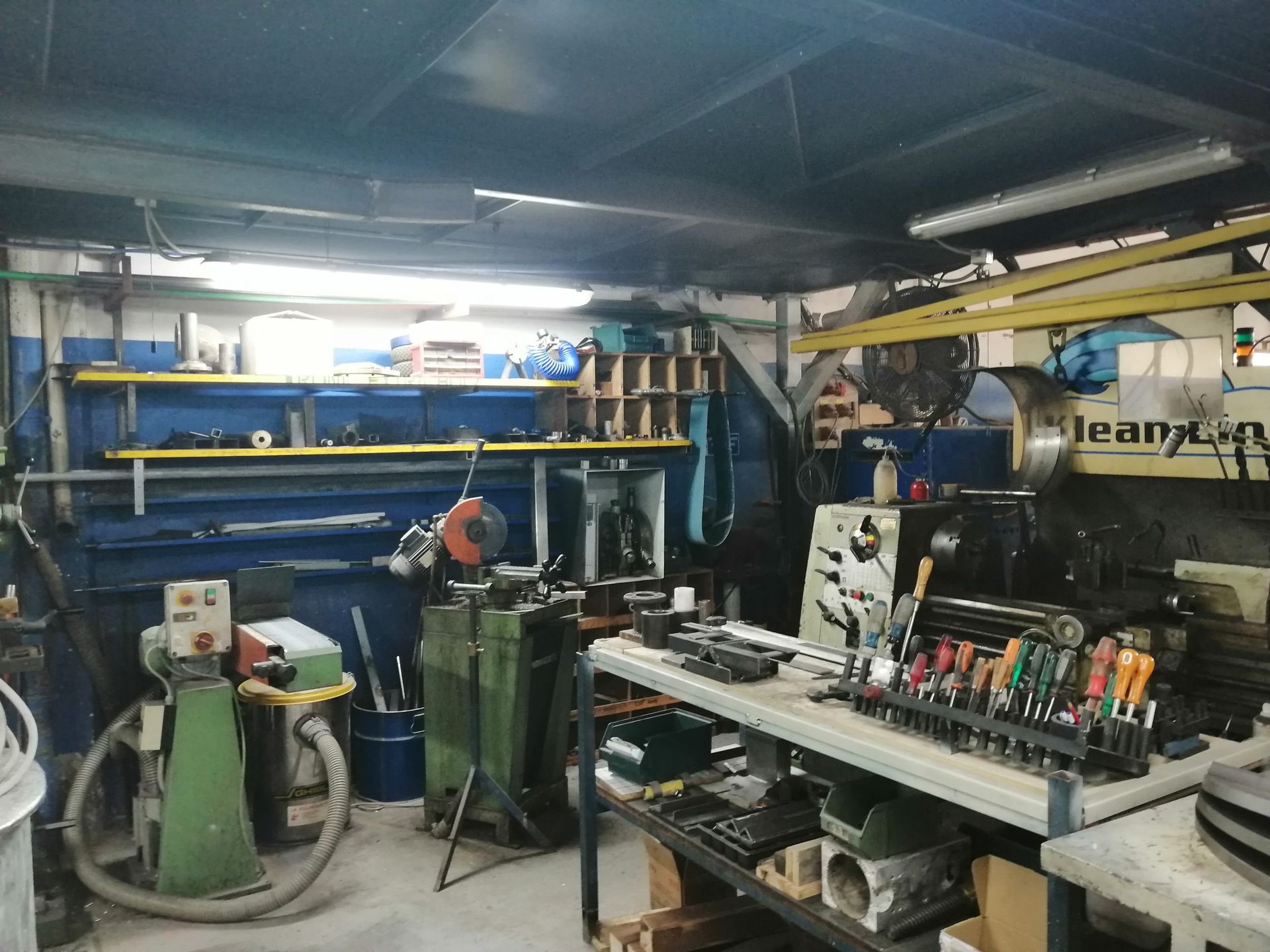 Interno dell'officina con utensili, scaffali, macchinari e vari articoli per la lavorazione dei metalli.