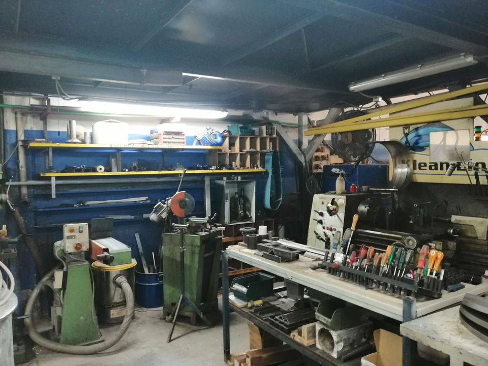 Interno dell'officina con utensili, scaffali, macchinari e vari articoli per la lavorazione dei metalli.