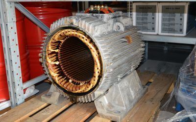 Grande motore elettrico smontato con avvolgimenti in rame esposti, su un pallet di legno in un'area di stoccaggio.