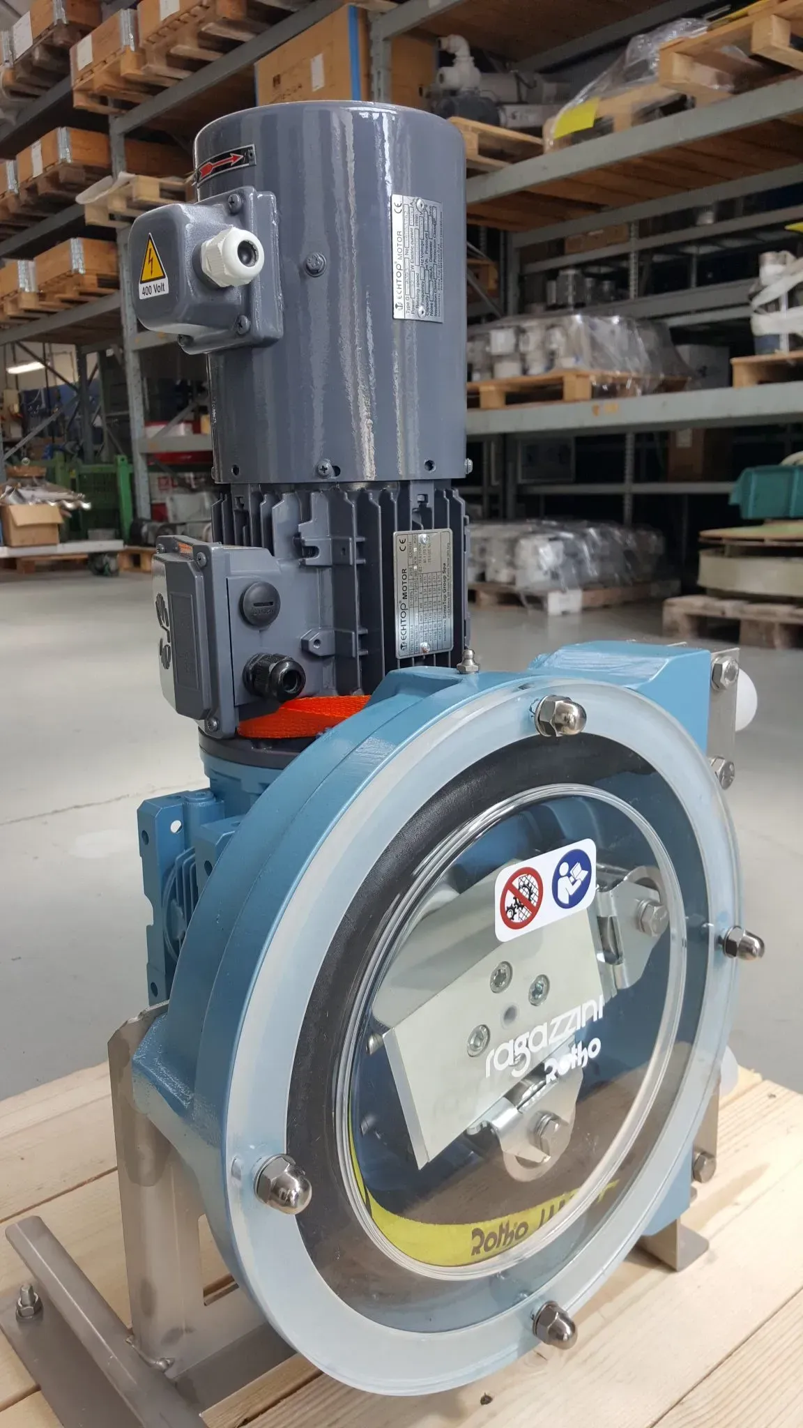 Pompa industriale con componenti blu e grigi, motore in alto, in un magazzino.