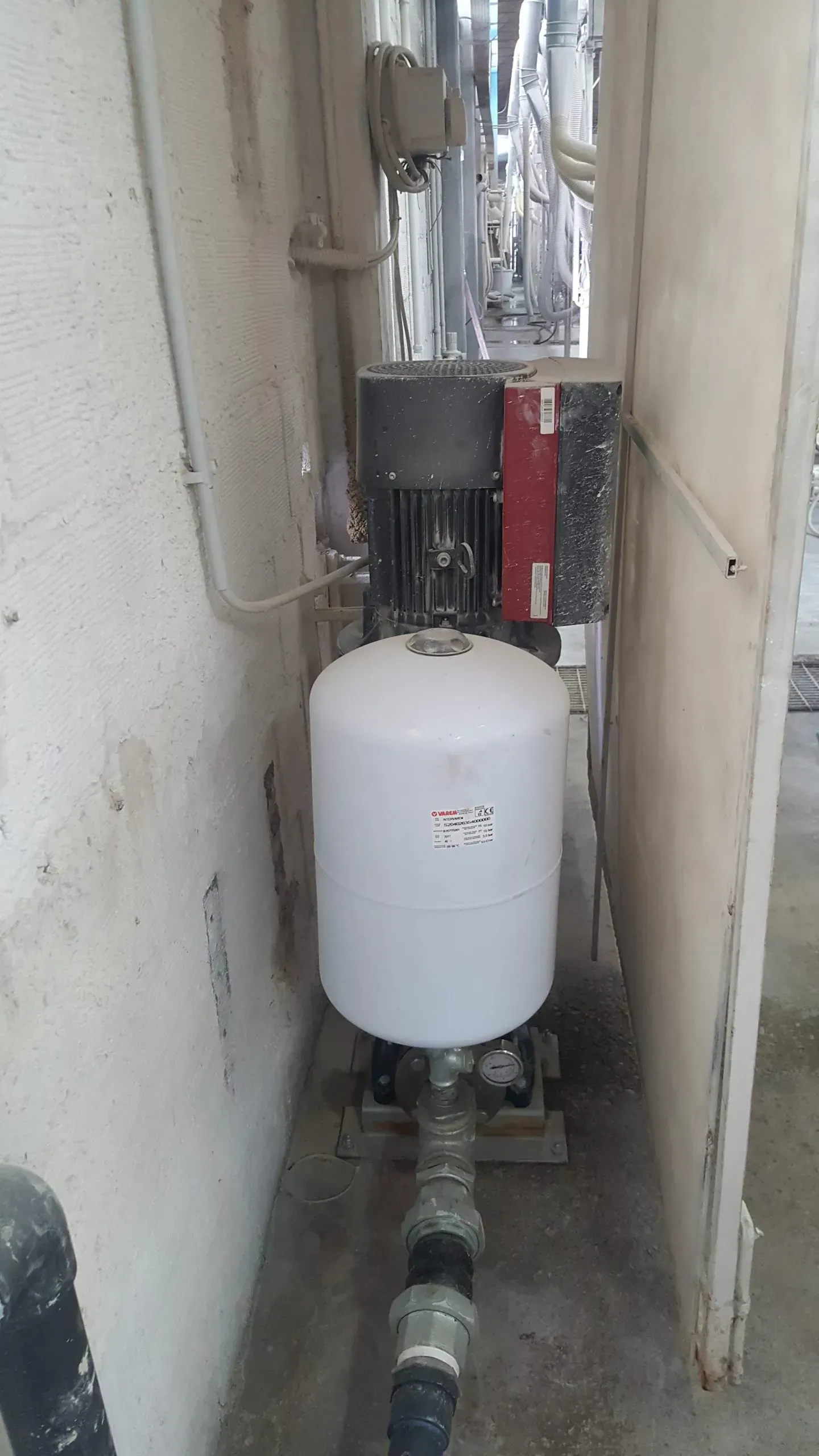 Sistema di pompaggio dell'acqua in un ripostiglio; serbatoio bianco, motore nero, tubi grigi.