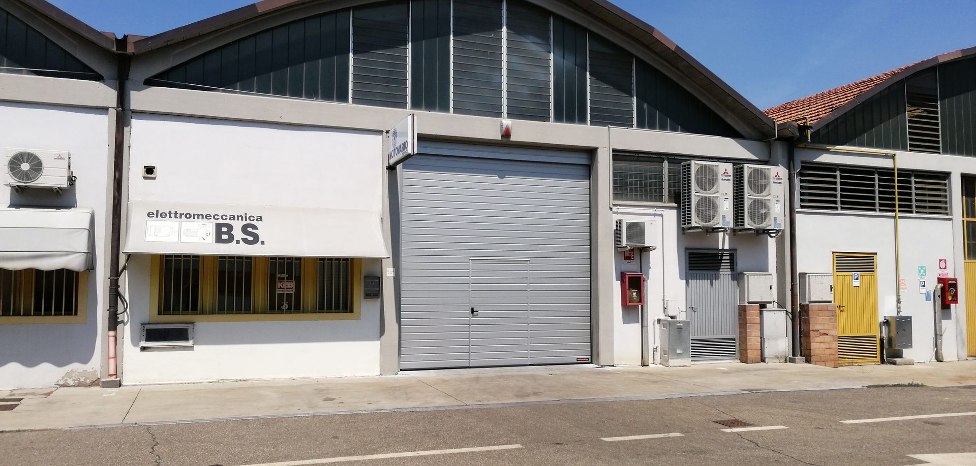 Un edificio commerciale con una porta avvolgibile e un cartello sopra una tenda da sole.