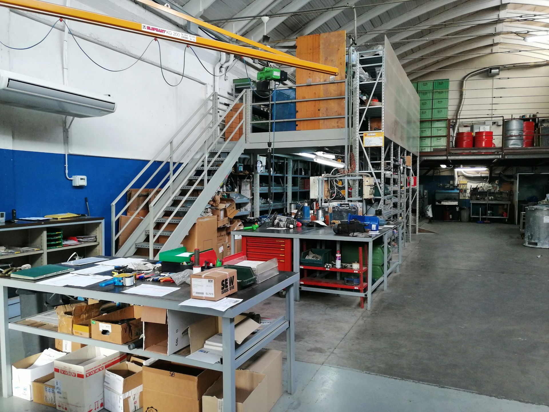 Interno di un magazzino con scaffalature, scale e banchi da lavoro ingombri di attrezzi e attrezzature.