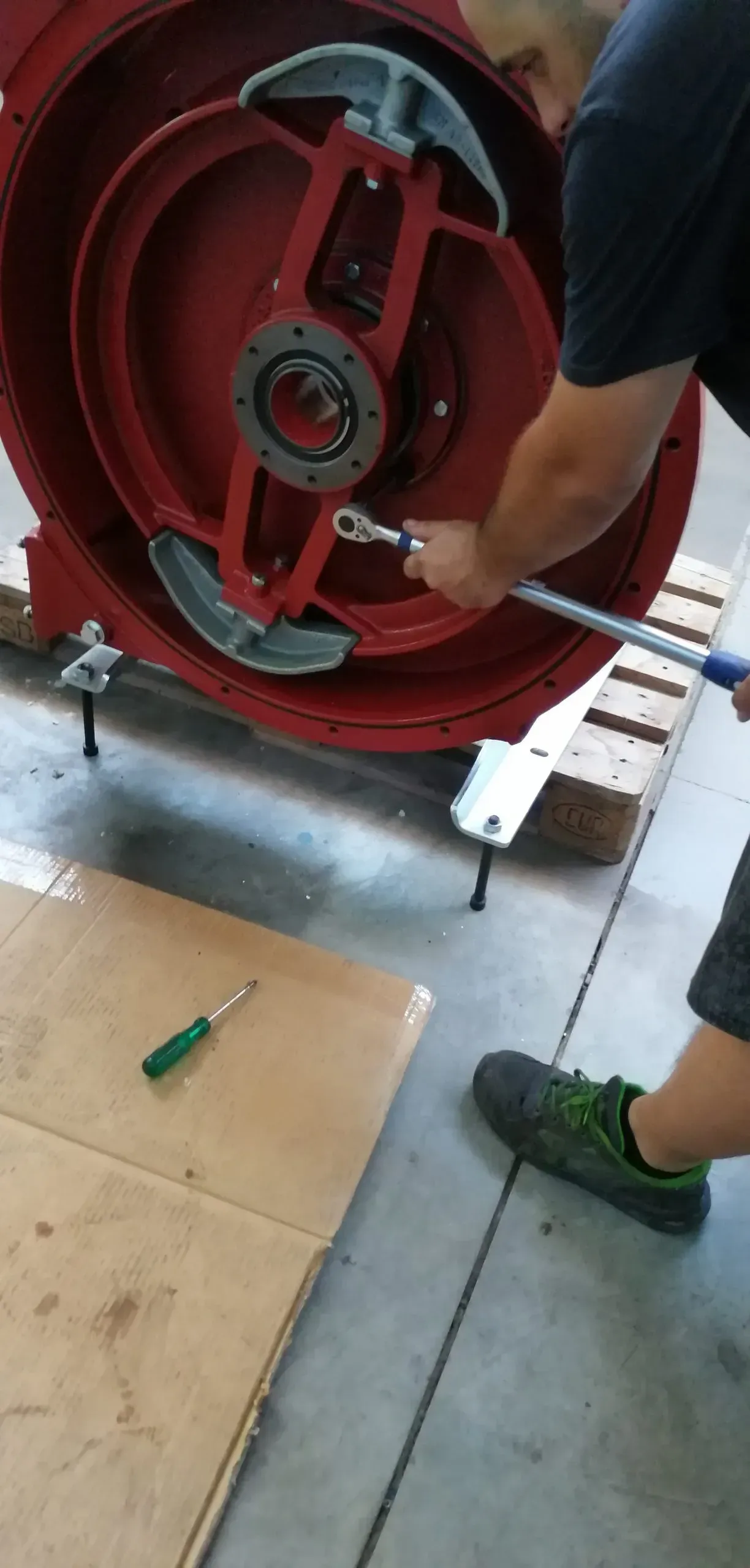 Una persona usa una chiave inglese su un macchinario rosso. Accanto a lei c'è un cacciavite appoggiato su un cartone.