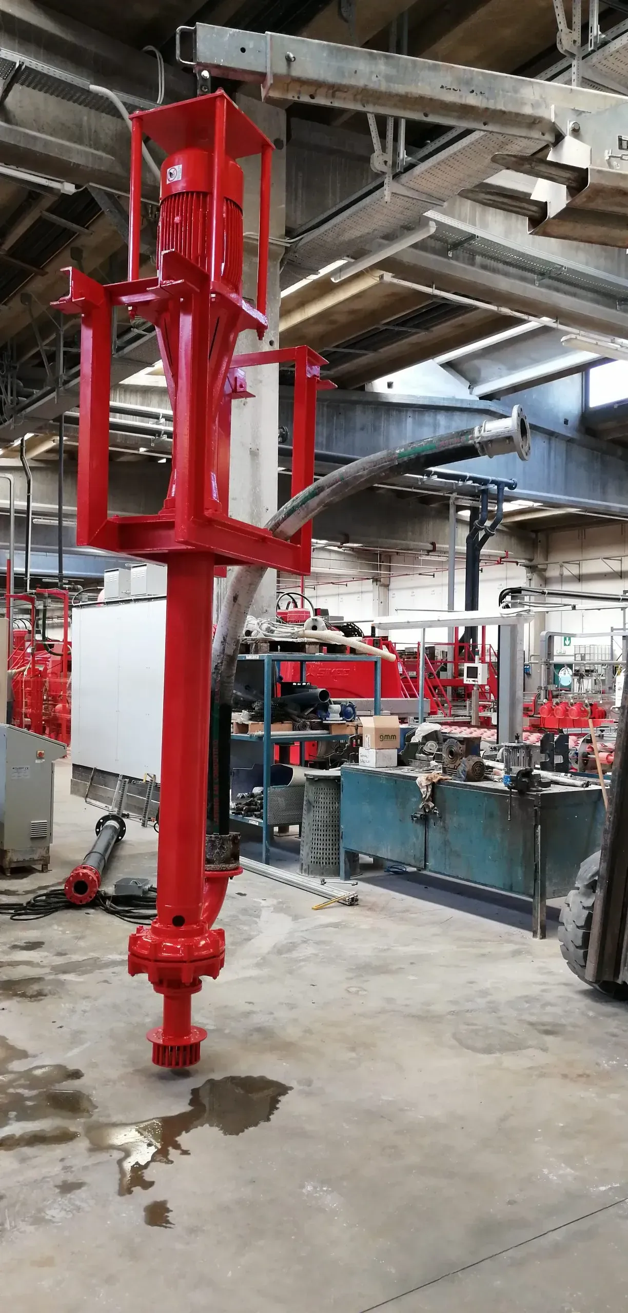 Macchinari industriali rossi in un'officina. Struttura verticale con telaio rettangolare, palo lungo e bracci multipli.