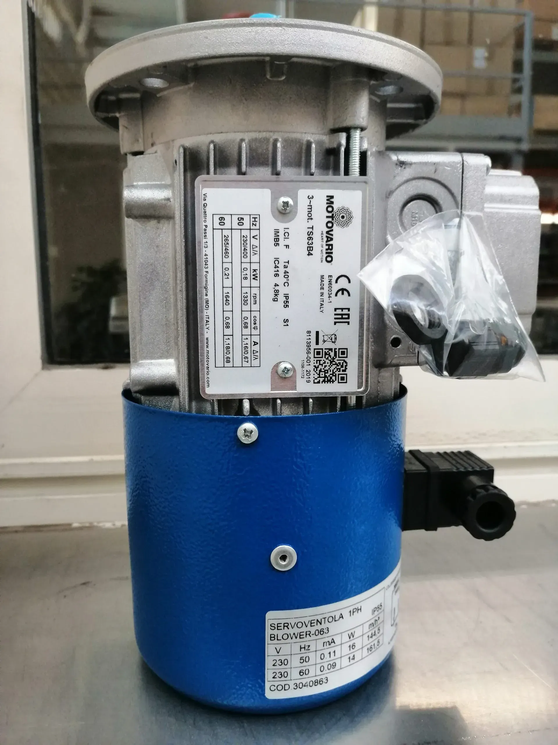 Motore elettrico, blu e argento, con componenti attaccati e un'etichetta; posizionato su una superficie.