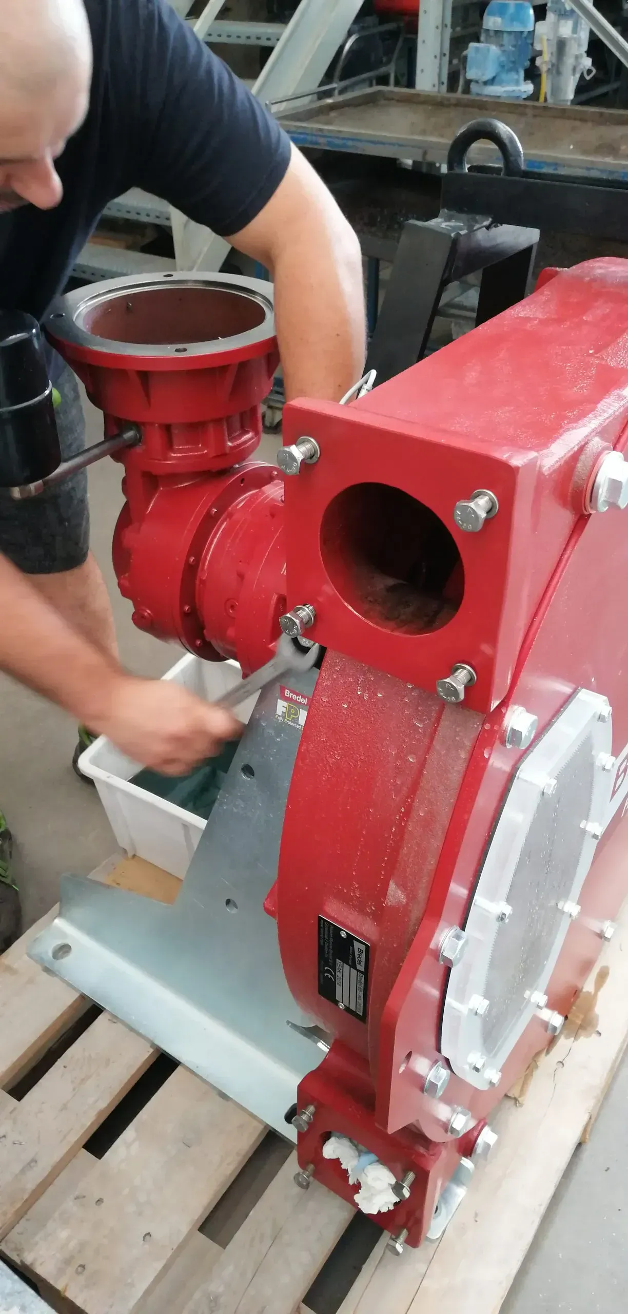 Persona che utilizza una chiave inglese per lavorare su una grande macchina industriale rossa, in un'officina.