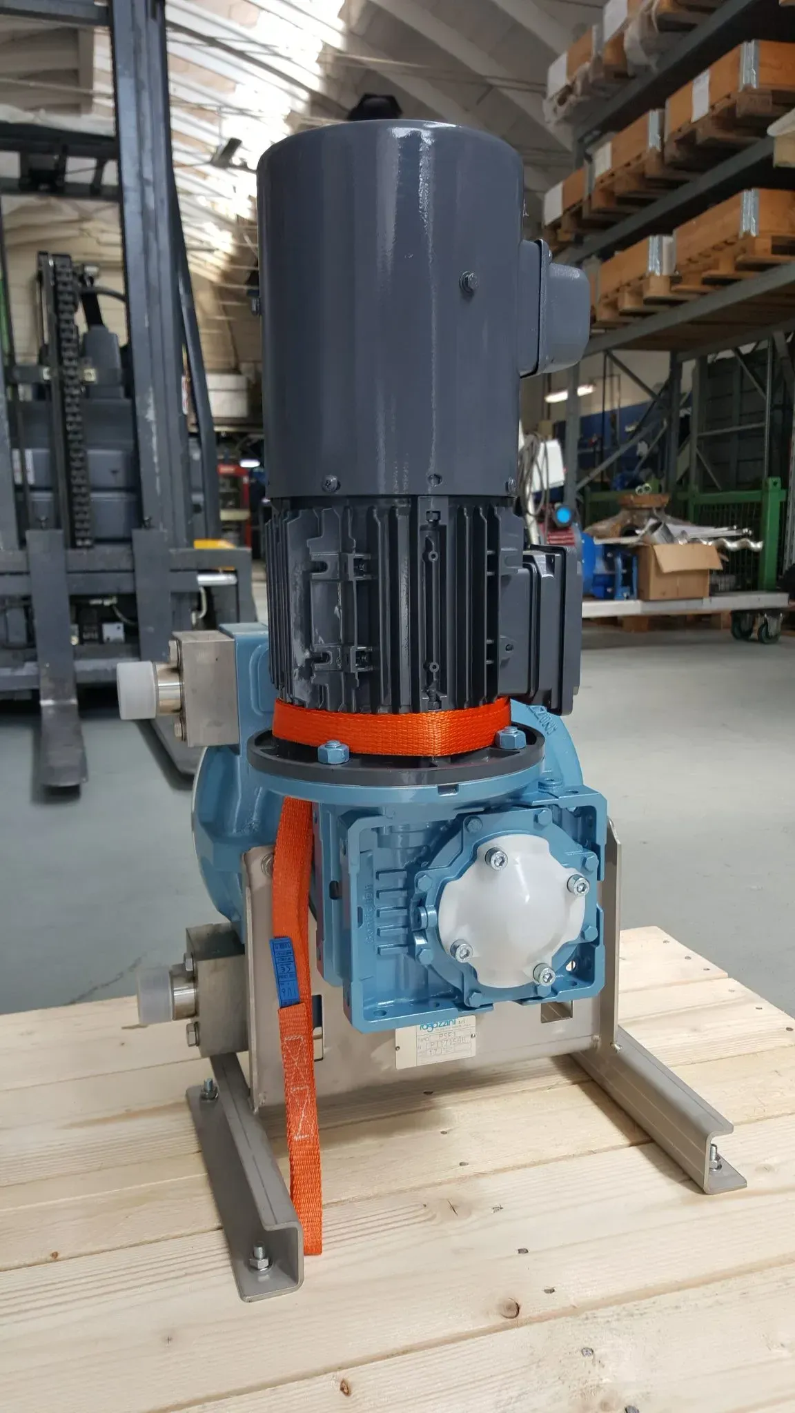 Gruppo motore e riduttore industriale blu su base metallica, cinghia arancione per fissarlo, installazione in magazzino.