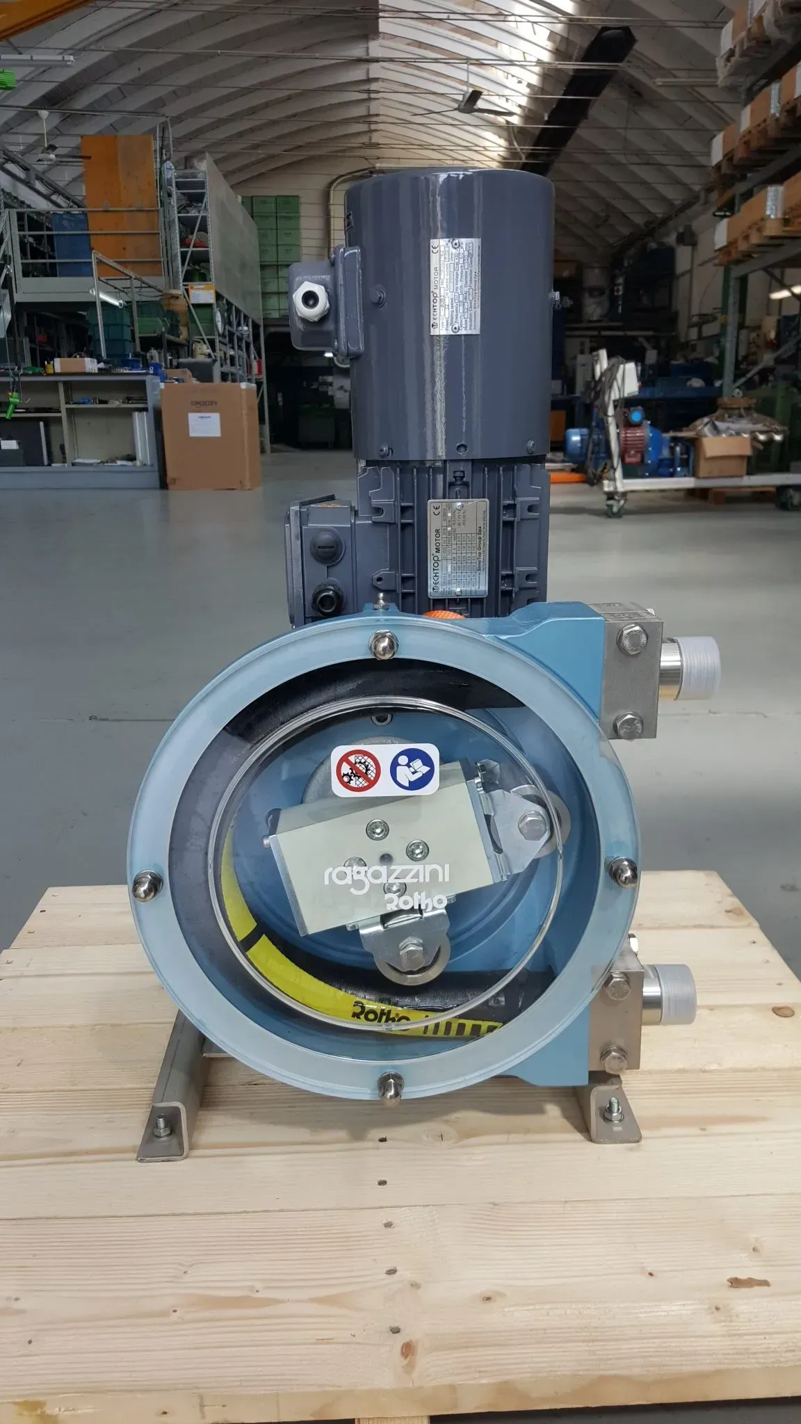 Pompa industriale blu con motore, su un pallet di legno in un magazzino.