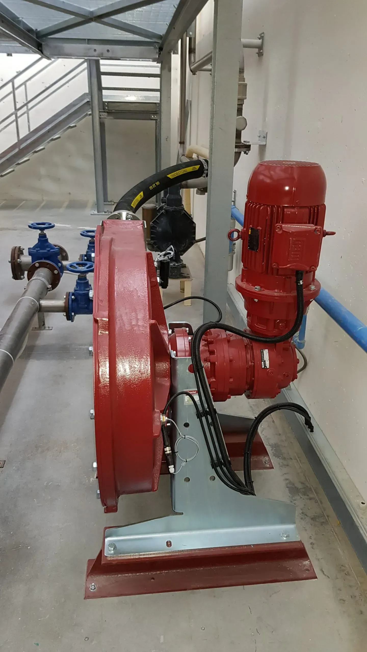 Pompa dell'acqua rossa con motore e tubature collegate in un ambiente industriale.