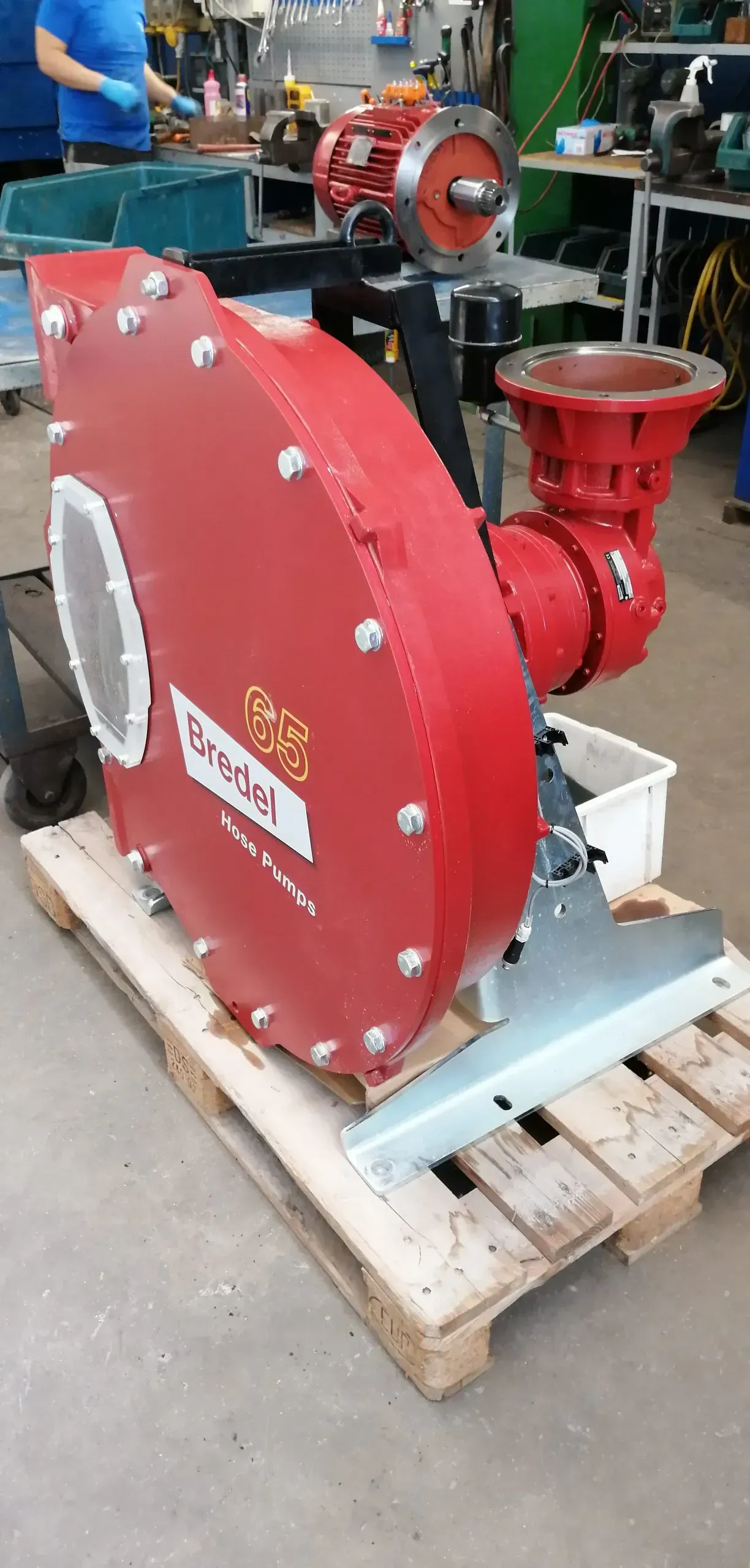 Ventilatore industriale rosso e gruppo motore su un pallet di legno in un'officina.