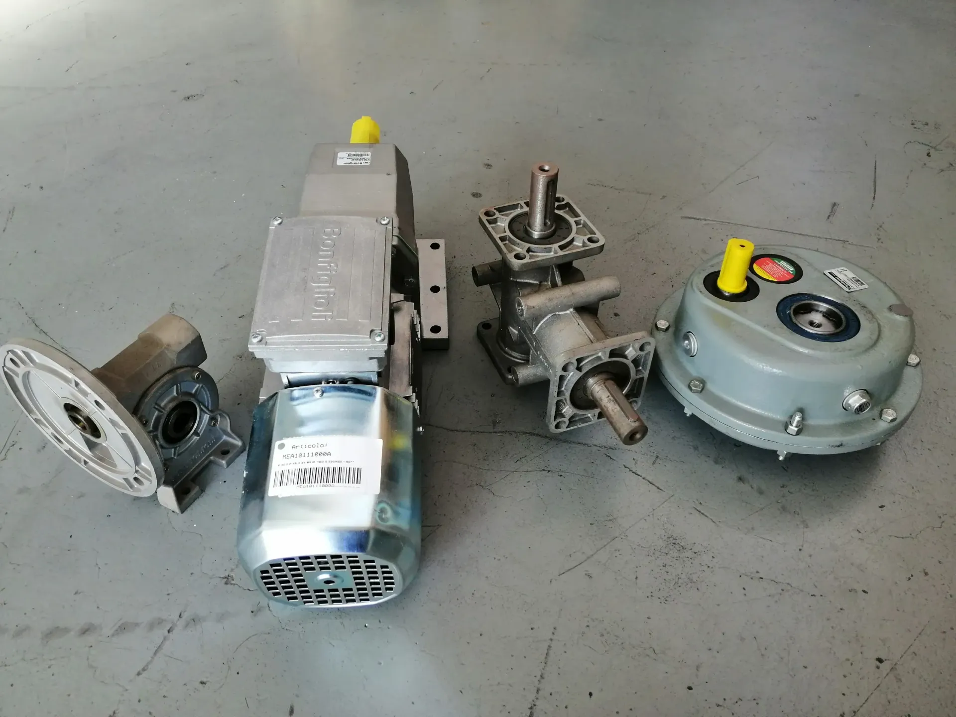 Su una superficie grigia sono presenti quattro riduttori industriali di vario tipo, color argento e grigio.