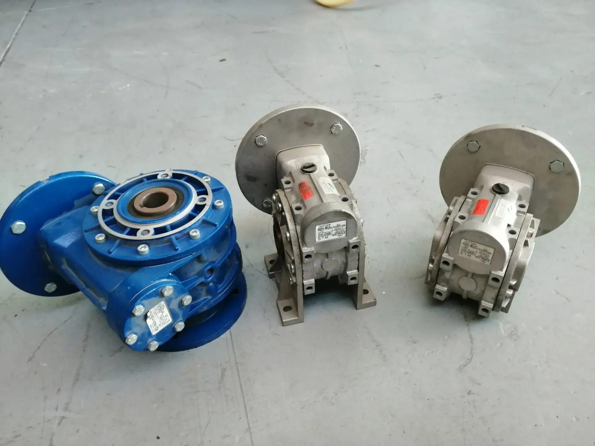 Tre riduttori industriali, blu e argento, su una superficie grigia.