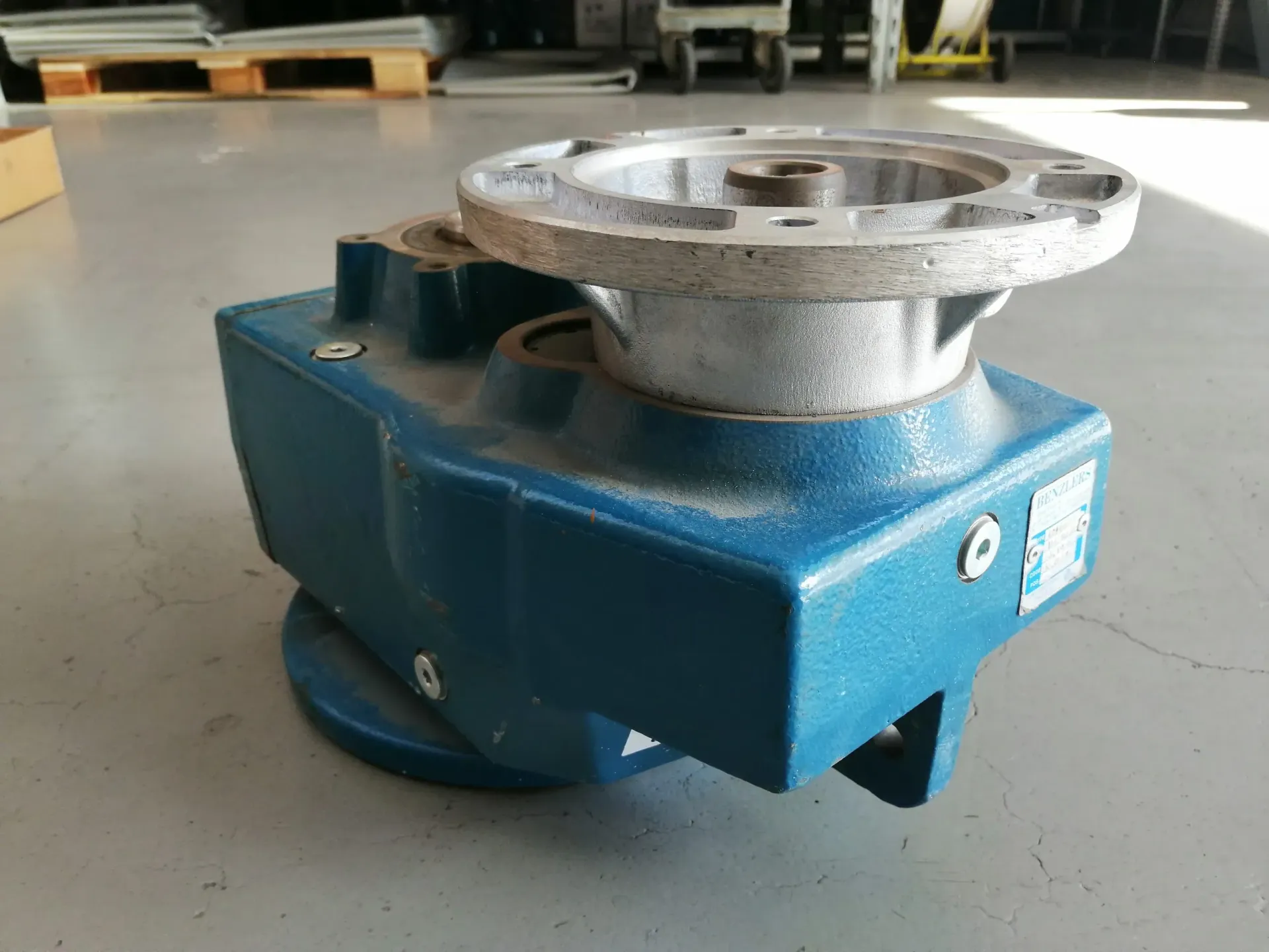 Scatola ingranaggi industriale blu con flangia argentata, appoggiata su un pavimento di cemento.