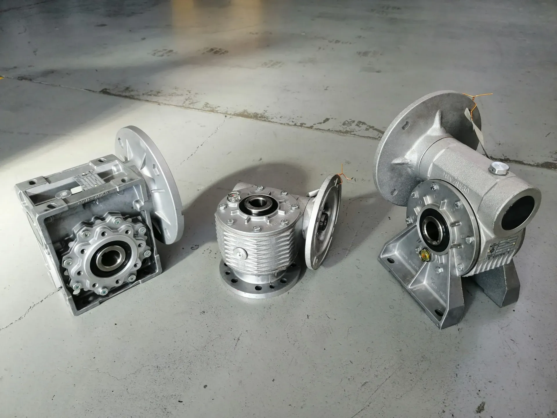 Tre riduttori industriali argentati su un pavimento di cemento.