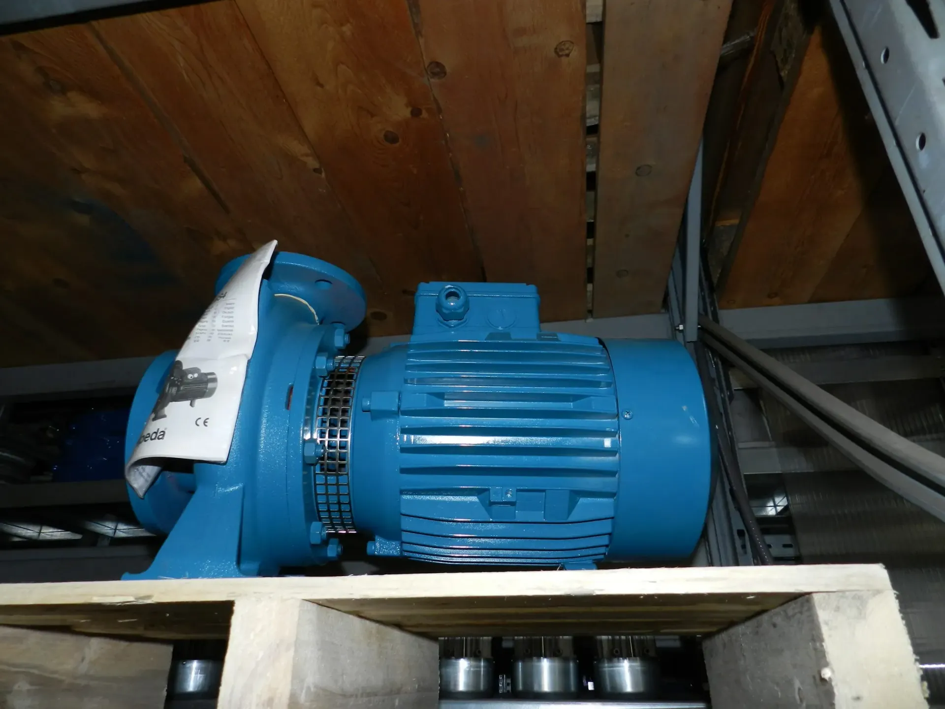 Motore elettrico blu appoggiato su un pallet, sotto uno scaffale di legno.