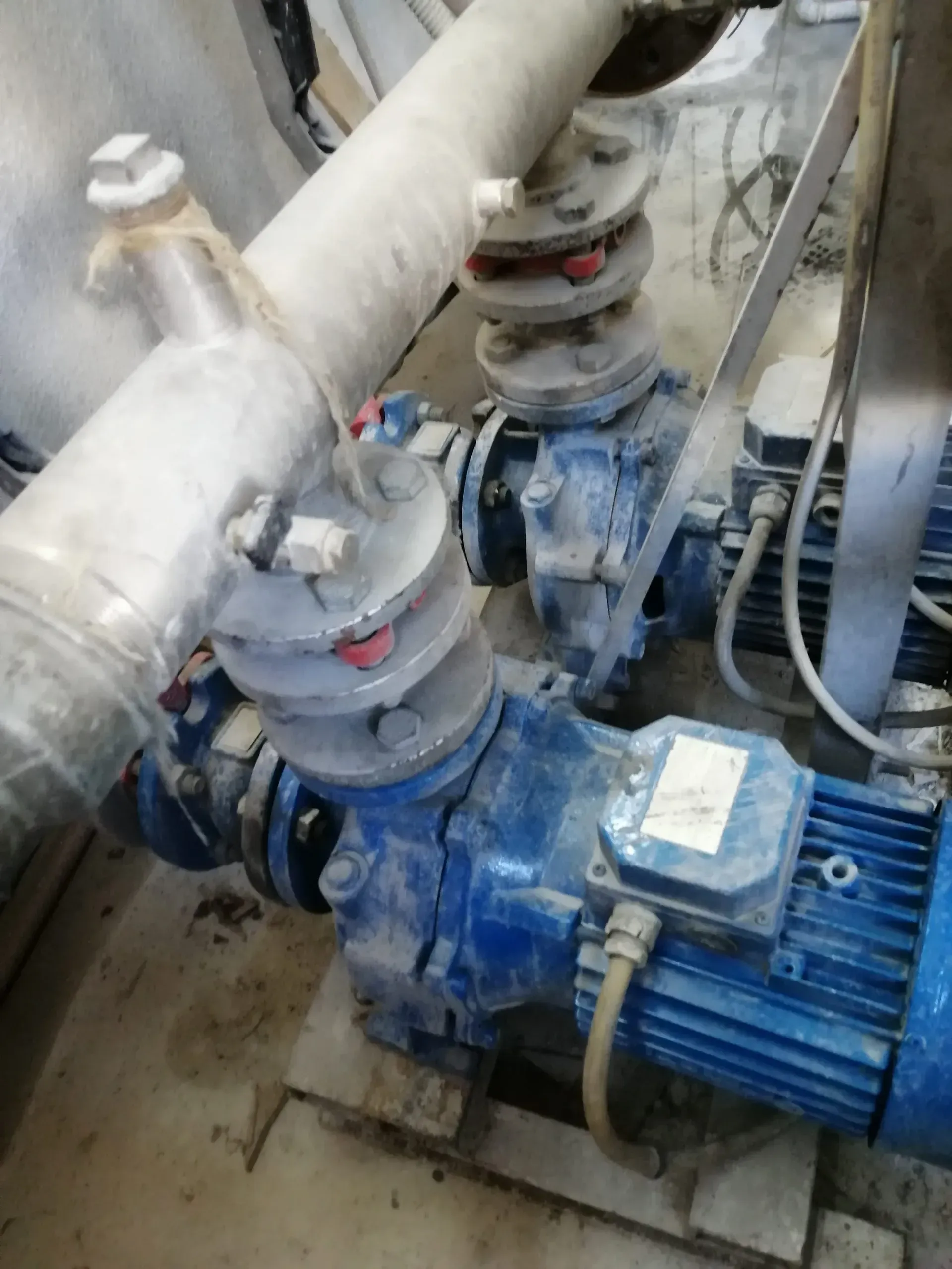 Pompe industriali blu con tubi e raccordi, al chiuso, coperte di polvere.