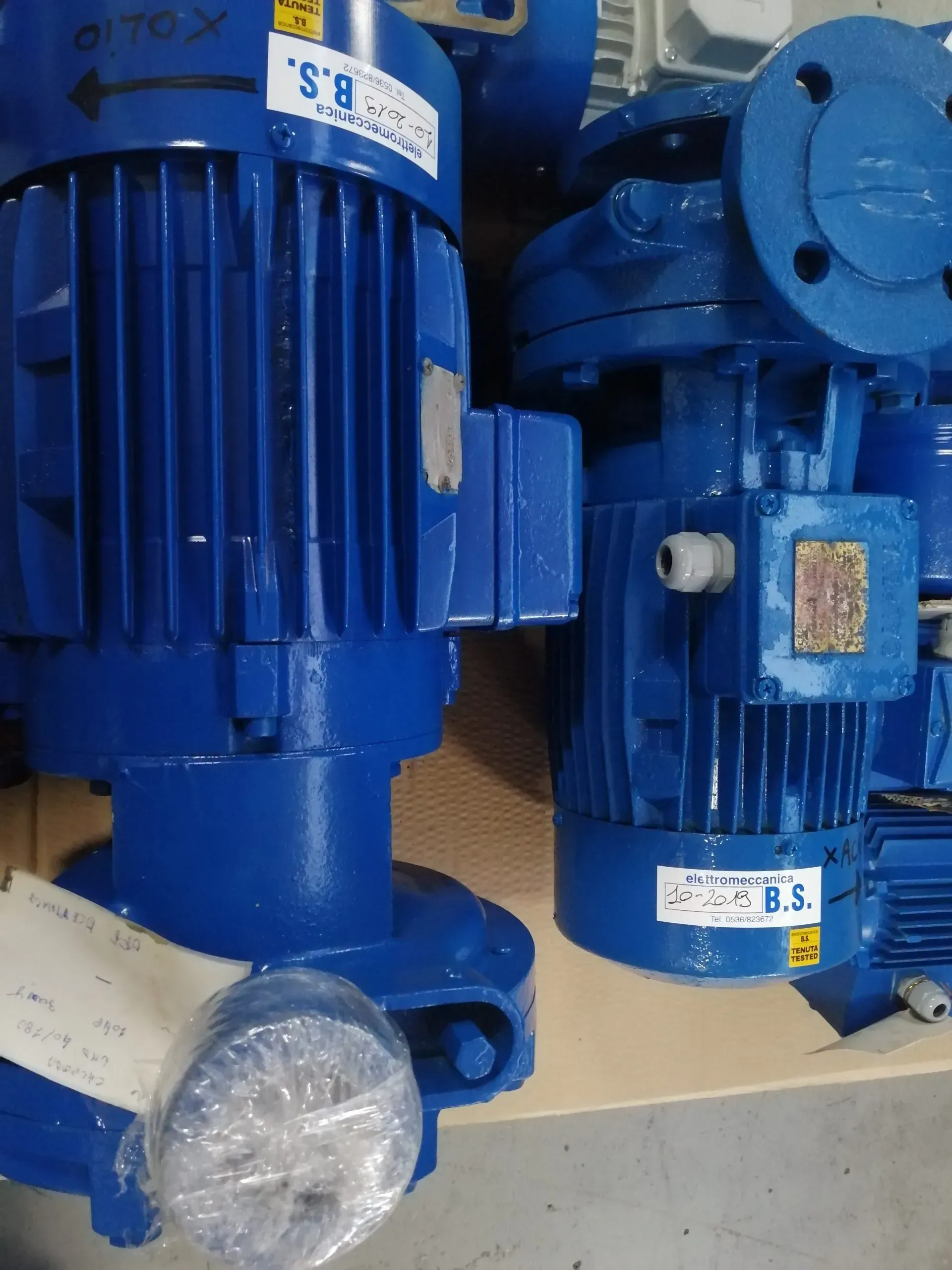 Due pompe industriali blu, una in primo piano. Etichette e bulloni visibili.