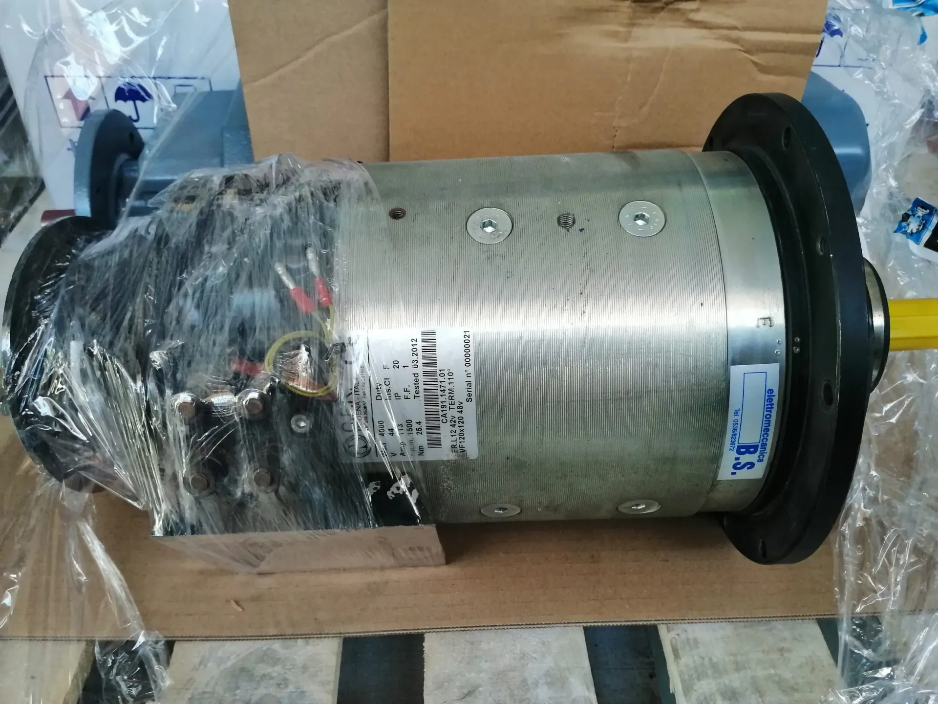 Motore cilindrico, avvolto in plastica, con albero giallo e flange nere, in una scatola.