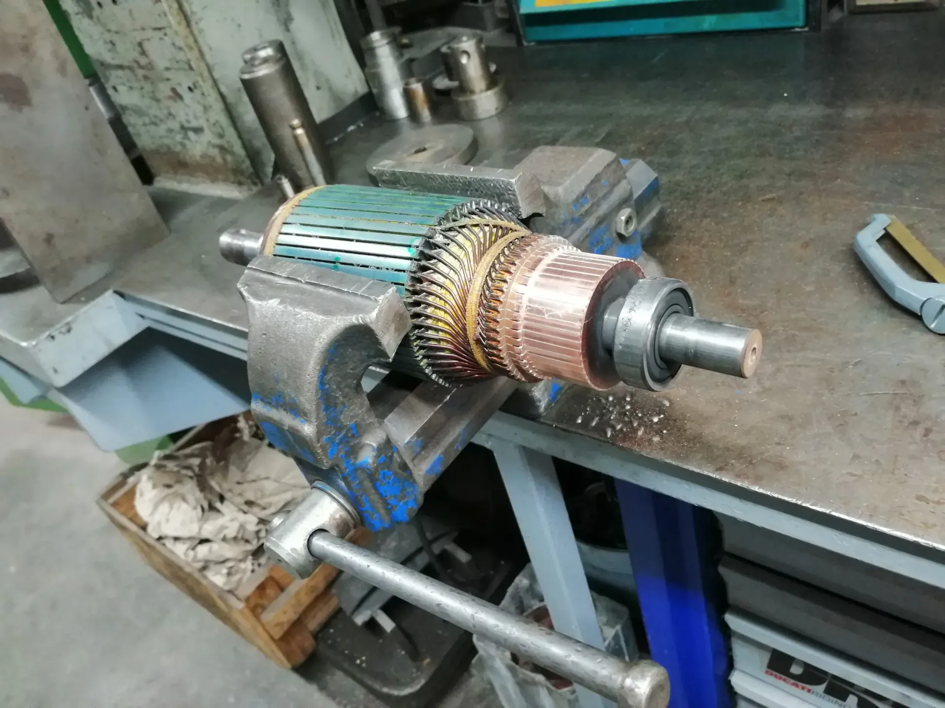 Indotto di un motore elettrico fissato in una morsa su un banco da lavoro, con avvolgimenti in rame e commutatore visibili.