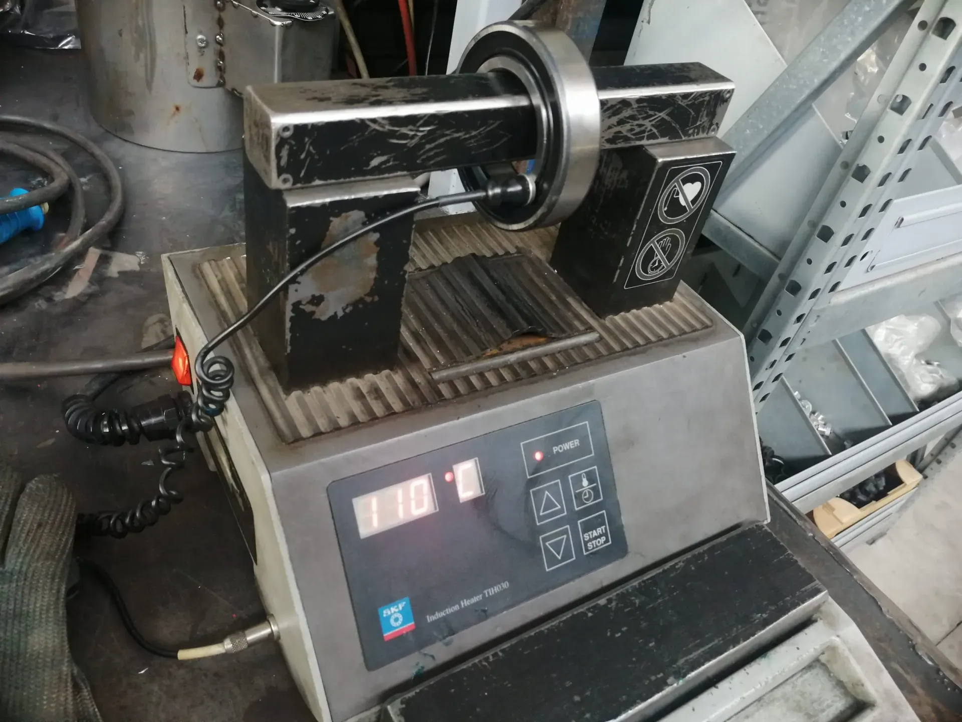 Un cuscinetto è posizionato su una macchina che visualizza 110,0. Un braccio metallico nero sostiene il cuscinetto.