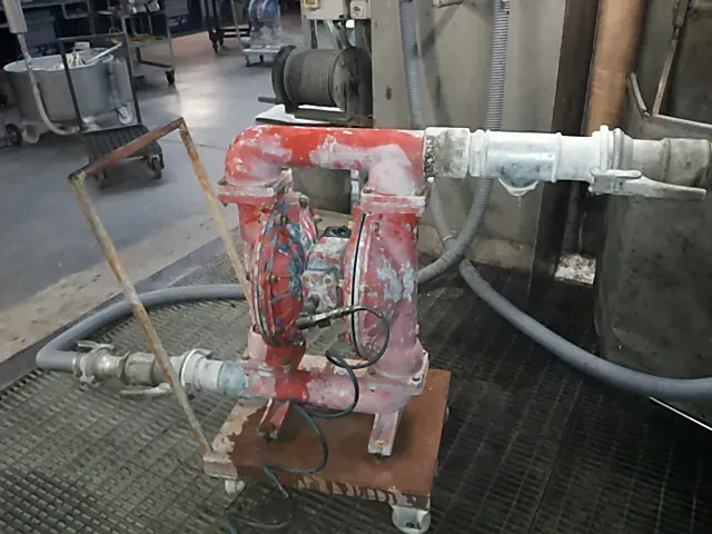 Pompa industriale rossa su una piattaforma di legno, collegata a tubi in un ambiente di fabbrica.