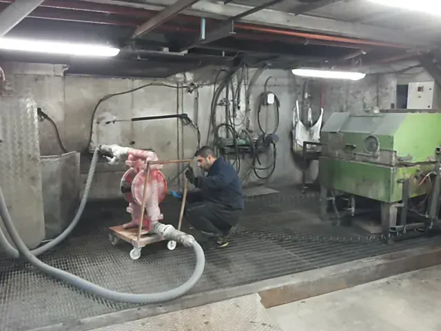 Un uomo lavora su una pompa rossa in un'officina di cemento con tubi flessibili e macchinari.