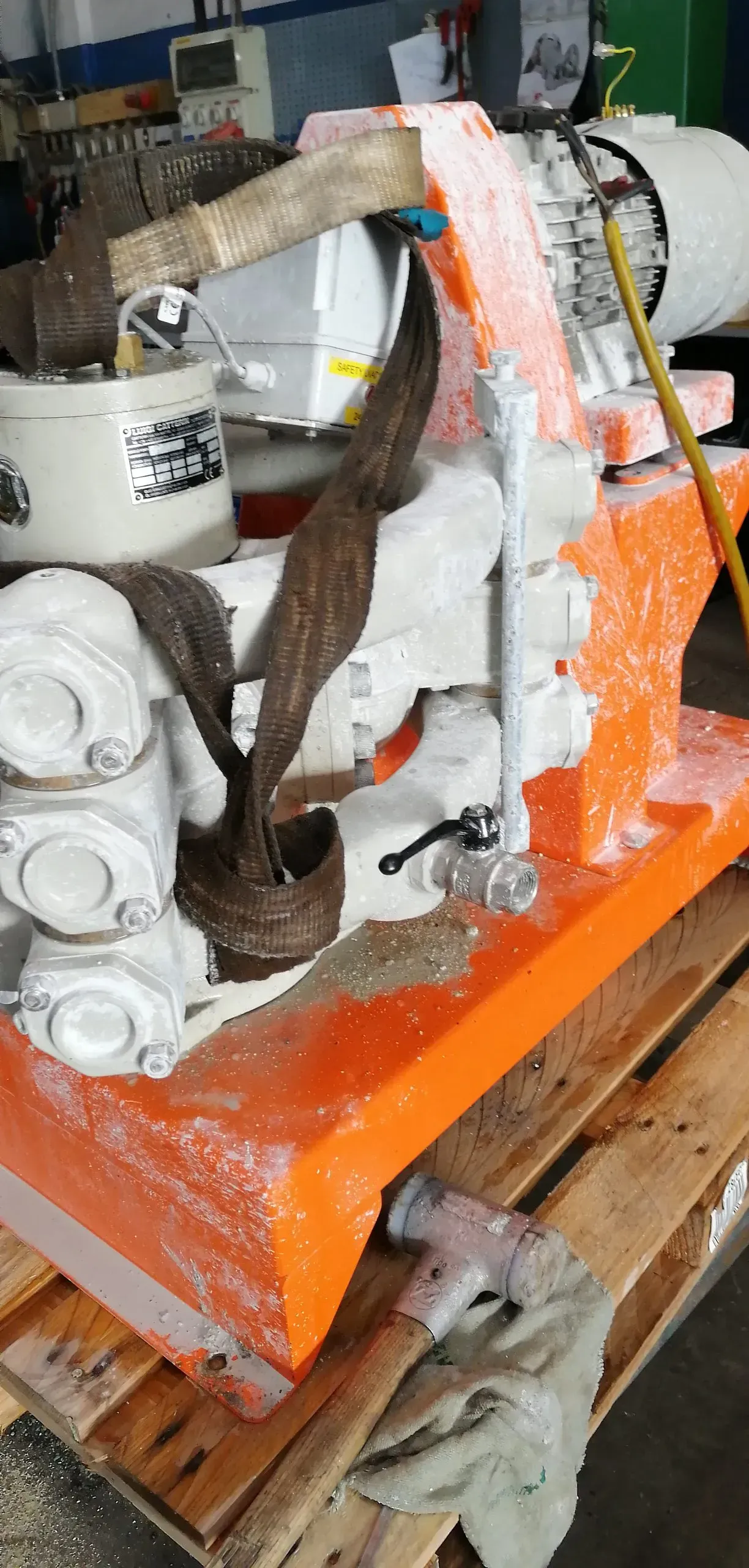 Un macchinario industriale, prevalentemente arancione e bianco, ricoperto da quello che sembra essere schiuma o materiale isolante, è posizionato su un pallet di legno.