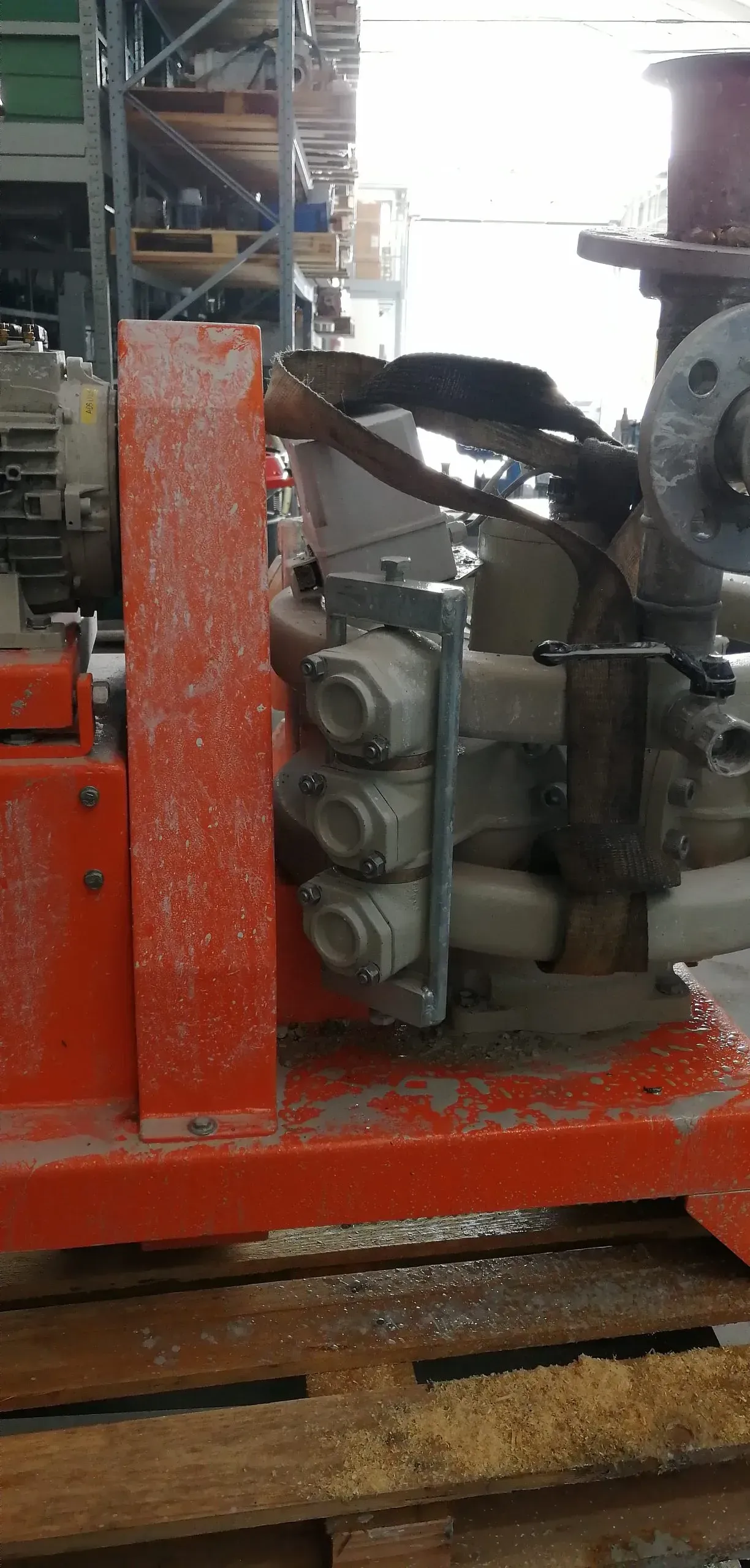 Primo piano di un macchinario industriale, probabilmente ambientato in un magazzino, con base e componenti in metallo rosso.