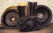 Parti della pompa in gomma nera, tra cui una voluta e una girante, su una superficie ruvida.