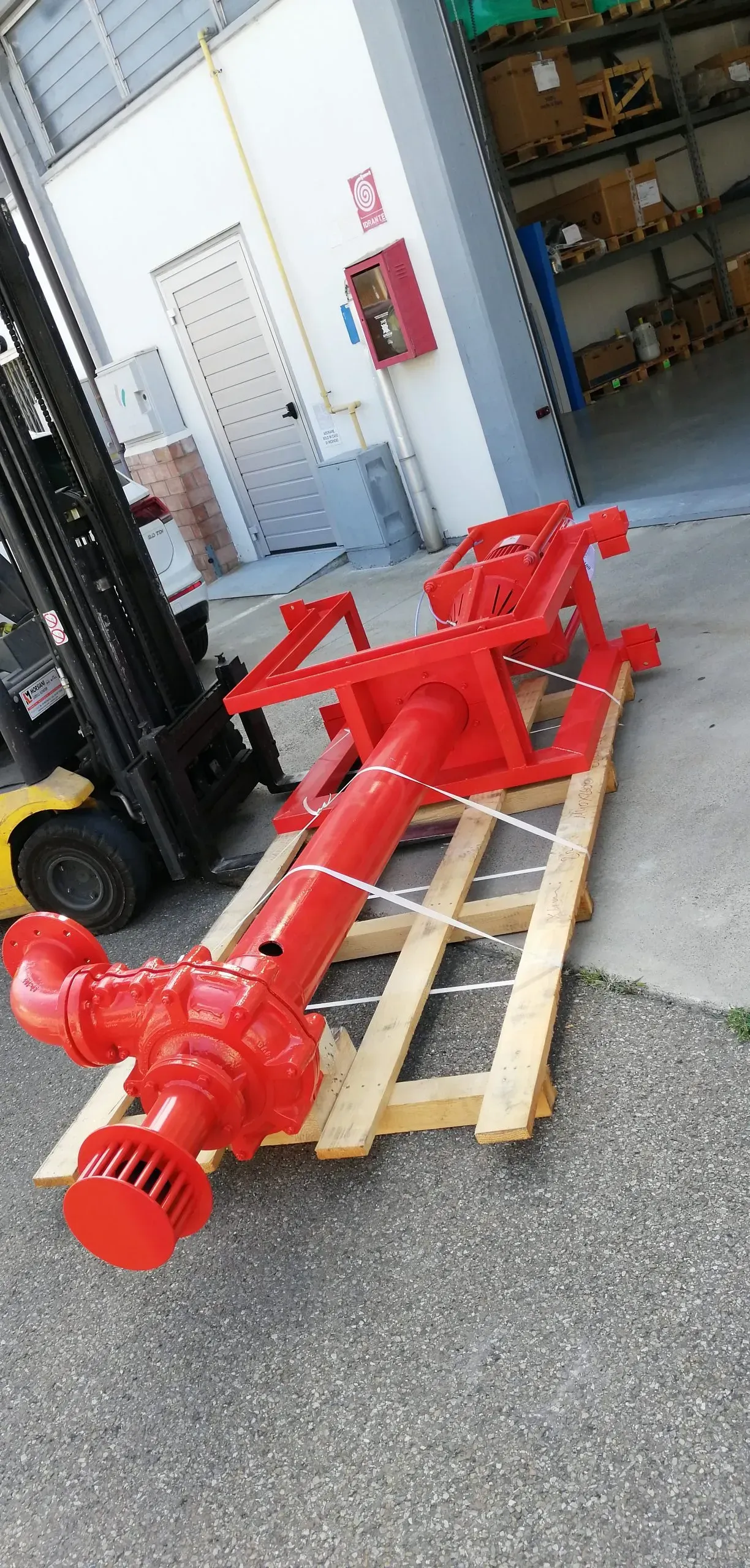 Pompa industriale rossa su un pallet di legno spostata da un carrello elevatore all'esterno di un edificio.