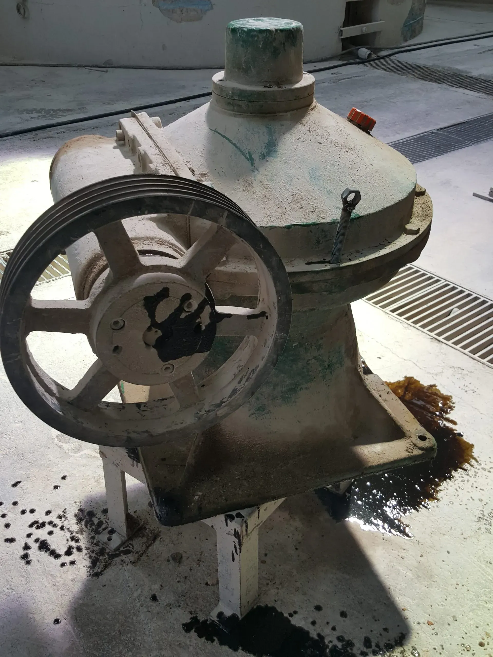 Un grande macchinario industriale usurato dalle intemperie, dotato di una puleggia, appoggiato su un pavimento di cemento.
