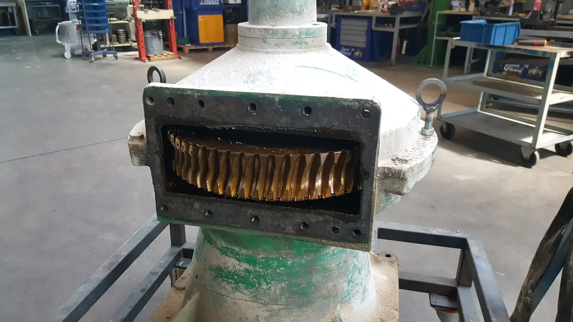 Macchina industriale verde con ingranaggi dorati a vista, in un ambiente da officina.