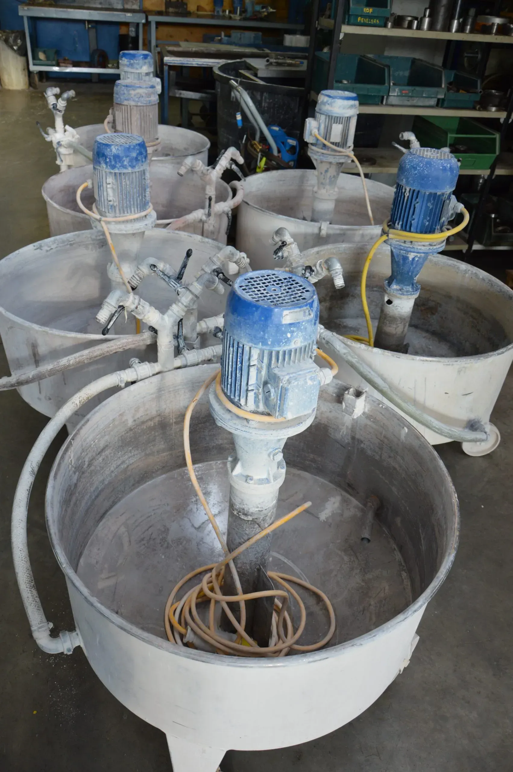 Diversi grandi miscelatori industriali con motori blu e vasche bianche, all'interno.