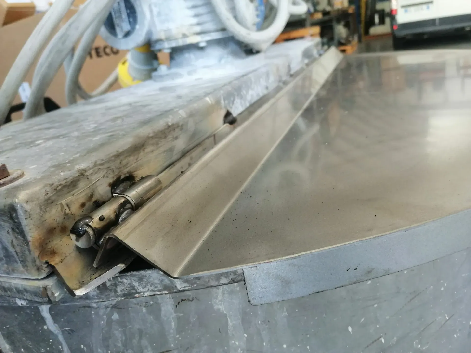 Sportello metallico incernierato a una macchina, appoggiato su una superficie grigia, all'interno.