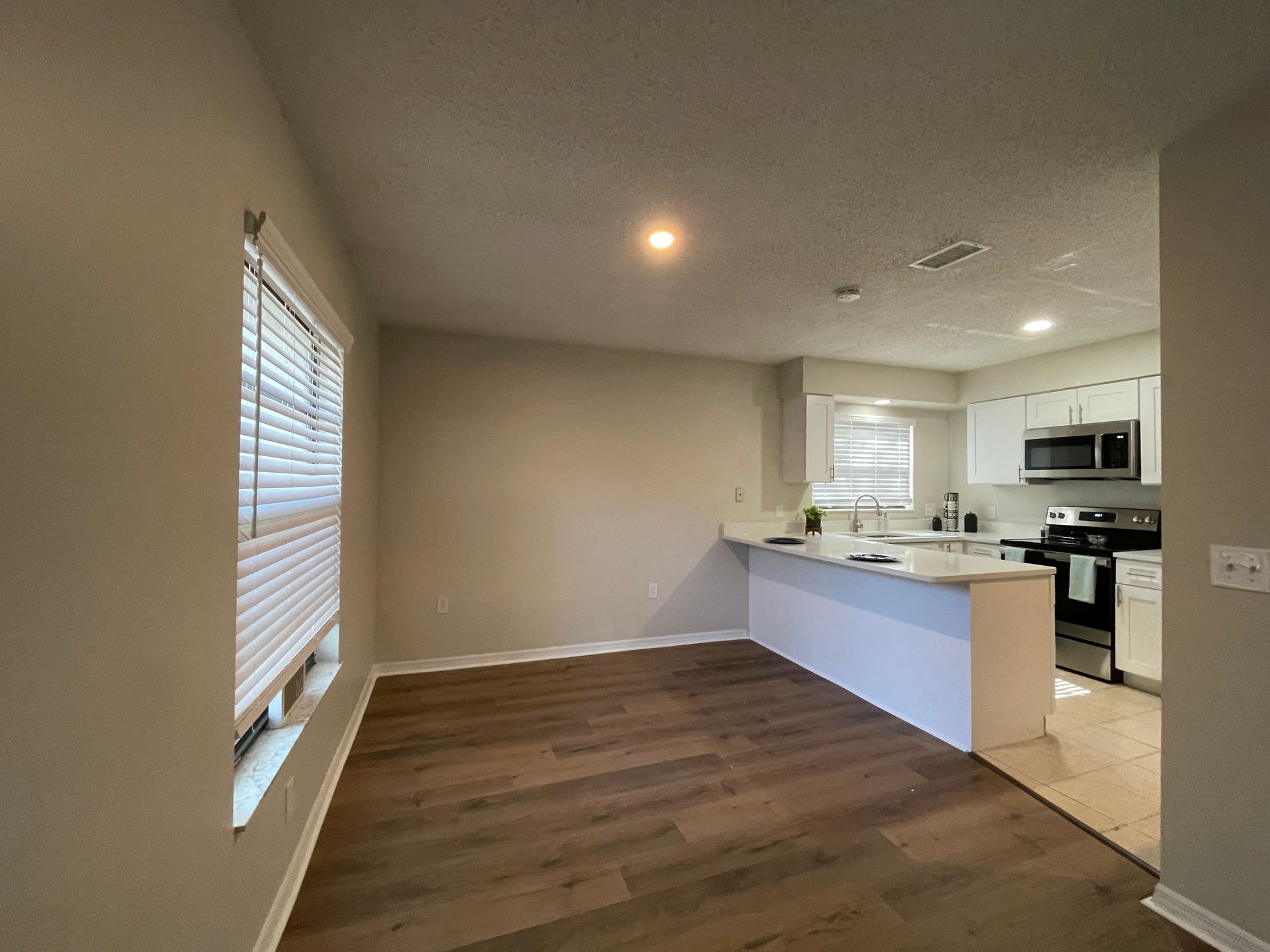 A living room with hardwood floors and a kitchen in the background.